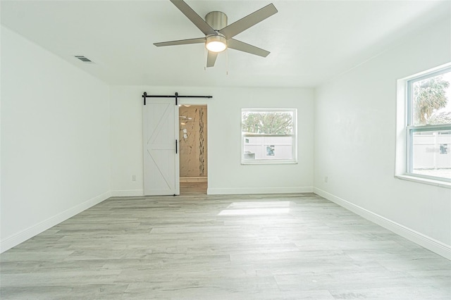 unfurnished room with ceiling fan, a barn door, and light hardwood / wood-style floors