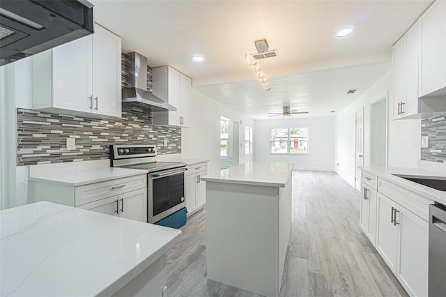 kitchen with wall chimney range hood, light hardwood / wood-style flooring, appliances with stainless steel finishes, a center island, and white cabinets