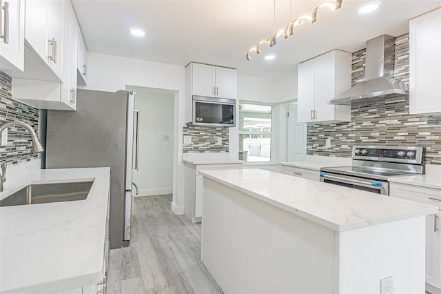 kitchen featuring pendant lighting, appliances with stainless steel finishes, white cabinets, a kitchen island, and wall chimney exhaust hood