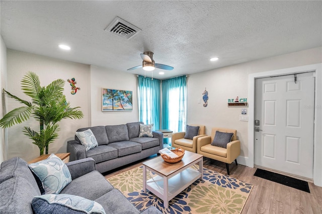 living room featuring ceiling fan, light hardwood / wood-style floors, and a textured ceiling