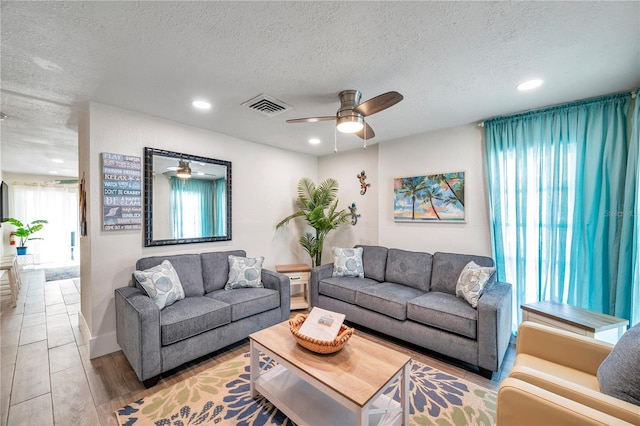 living room featuring ceiling fan, light hardwood / wood-style flooring, and a textured ceiling