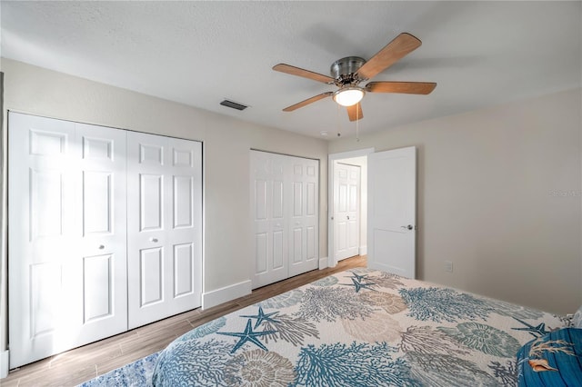 bedroom featuring multiple closets, ceiling fan, and light hardwood / wood-style flooring