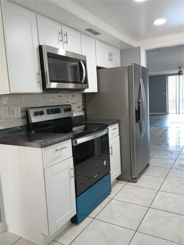 kitchen with stainless steel appliances, light tile patterned floors, white cabinets, and backsplash