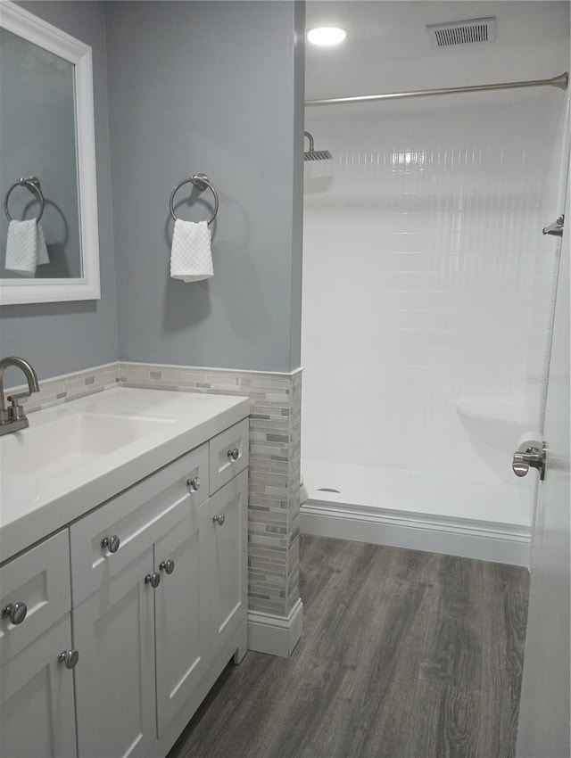 bathroom with hardwood / wood-style flooring, vanity, walk in shower, and tile walls