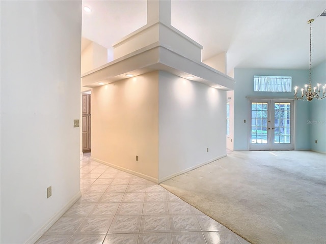 carpeted empty room with a towering ceiling, a notable chandelier, and french doors