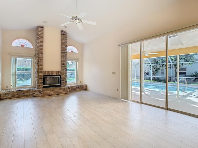 unfurnished living room with high vaulted ceiling, a brick fireplace, a wealth of natural light, and ceiling fan