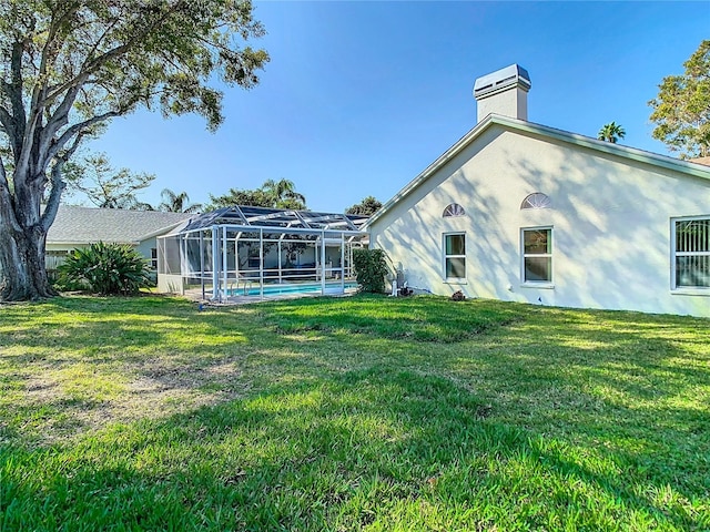 rear view of house with glass enclosure and a lawn