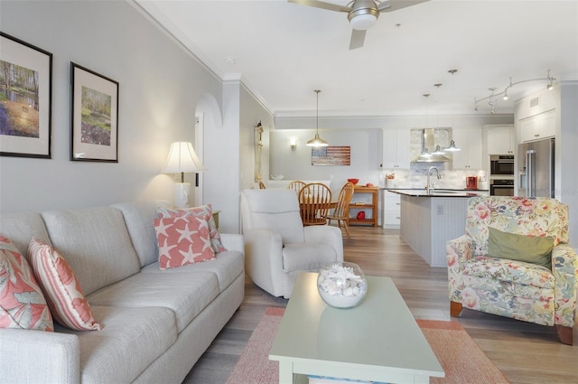 living area with light wood-style floors, arched walkways, ornamental molding, and ceiling fan