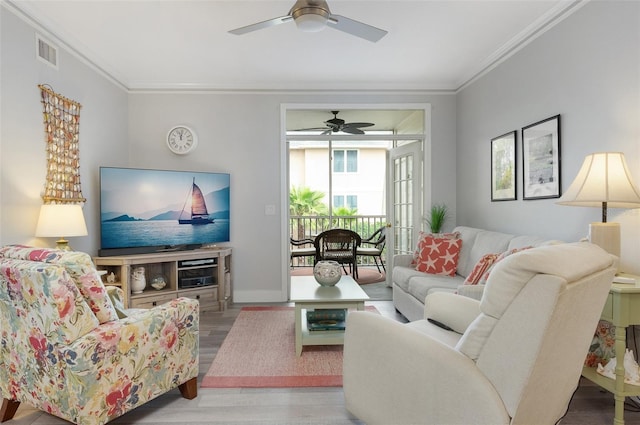 living room featuring ceiling fan, visible vents, crown molding, and wood finished floors