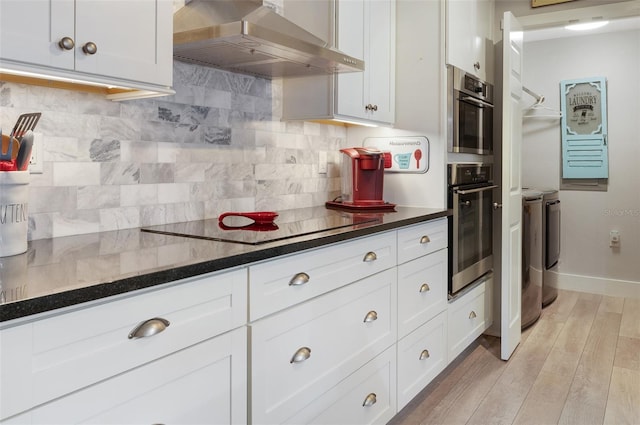 kitchen with dark countertops, range hood, white cabinetry, and separate washer and dryer