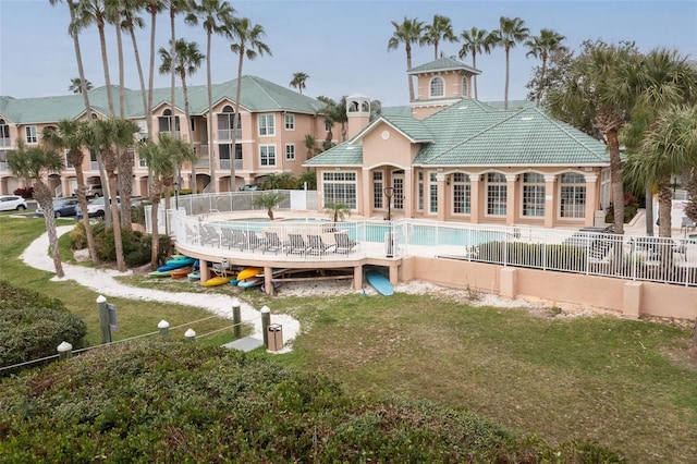 back of house featuring a lawn, a fenced in pool, a tile roof, fence, and stucco siding