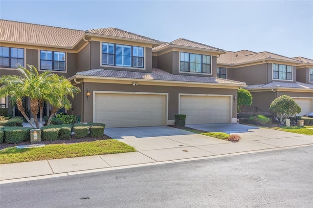 view of front facade with a garage, concrete driveway, a tile roof, and stucco siding