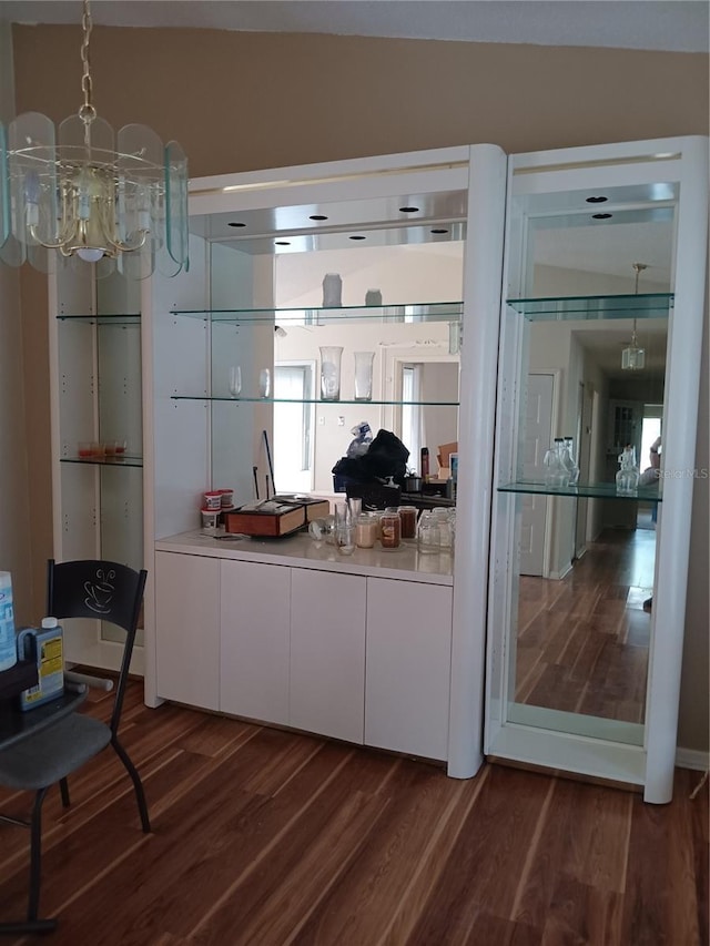 bar featuring dark hardwood / wood-style flooring, a chandelier, and white cabinets