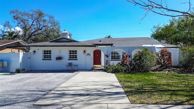 ranch-style home featuring driveway, a front yard, fence, and stucco siding