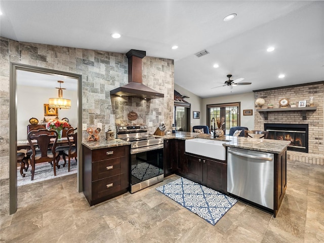 kitchen featuring sink, stainless steel appliances, wall chimney exhaust hood, kitchen peninsula, and a fireplace