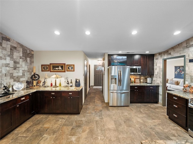 kitchen featuring appliances with stainless steel finishes, dark brown cabinets, light stone counters, and tasteful backsplash