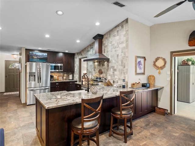 kitchen featuring dark brown cabinets, stainless steel appliances, kitchen peninsula, and wall chimney range hood