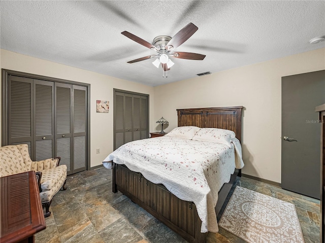 bedroom with ceiling fan, two closets, and a textured ceiling