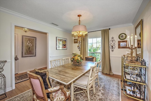 dining space with light wood-type flooring, crown molding, and a textured ceiling