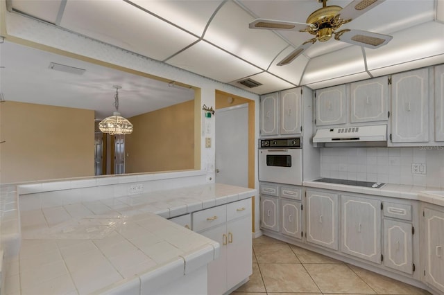 kitchen with white oven, tile counters, visible vents, white cabinets, and under cabinet range hood