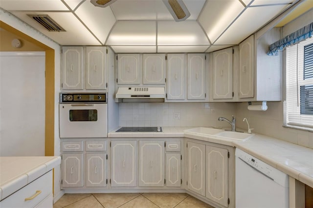 kitchen featuring white appliances, a sink, under cabinet range hood, and tile countertops