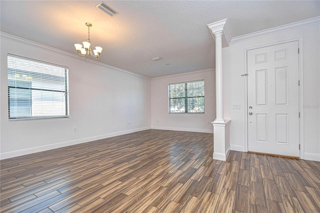 foyer entrance featuring an inviting chandelier, ornamental molding, decorative columns, and dark hardwood / wood-style floors