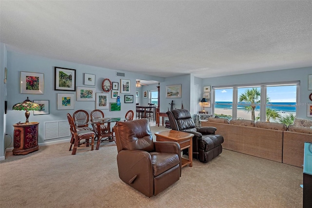 carpeted living room featuring a water view, ceiling fan, a textured ceiling, and a wealth of natural light