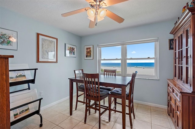 tiled dining space featuring ceiling fan, a textured ceiling, and a water view