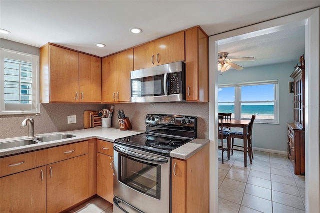 kitchen featuring appliances with stainless steel finishes, sink, light tile patterned floors, a water view, and a healthy amount of sunlight