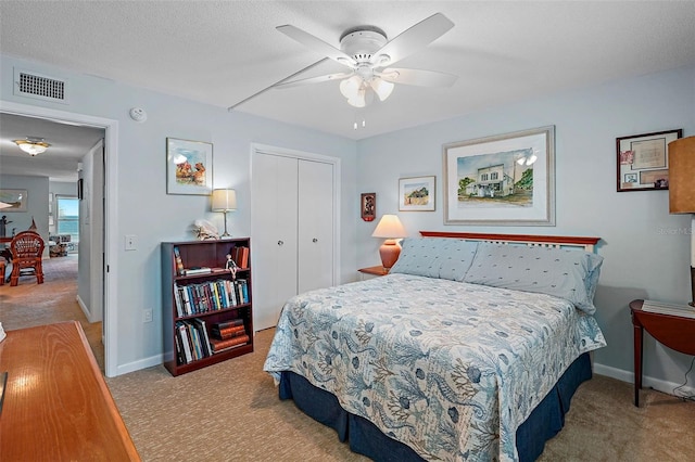 bedroom with light carpet, ceiling fan, a closet, and a textured ceiling