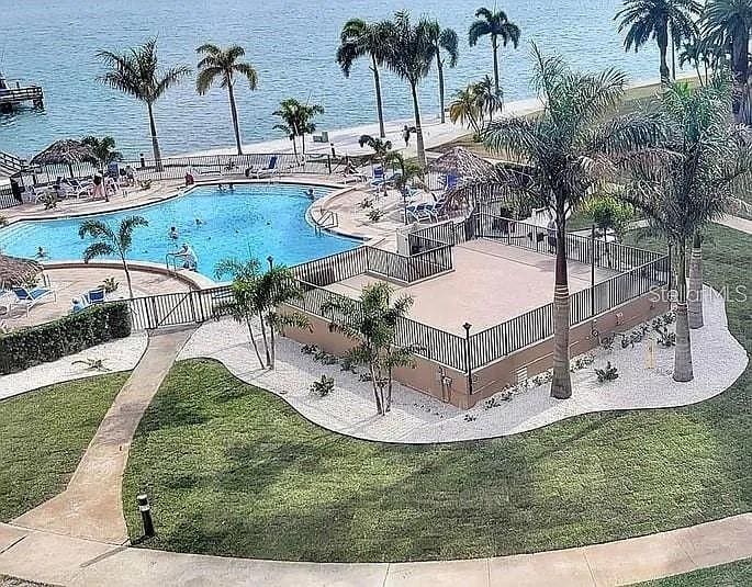 community pool with a water view, fence, a lawn, and a patio