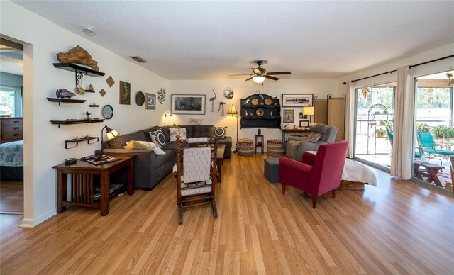 living room featuring visible vents, light wood-style flooring, a textured ceiling, and ceiling fan