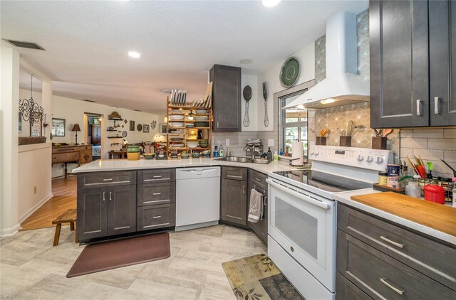 kitchen with white appliances, a peninsula, island exhaust hood, a sink, and light countertops