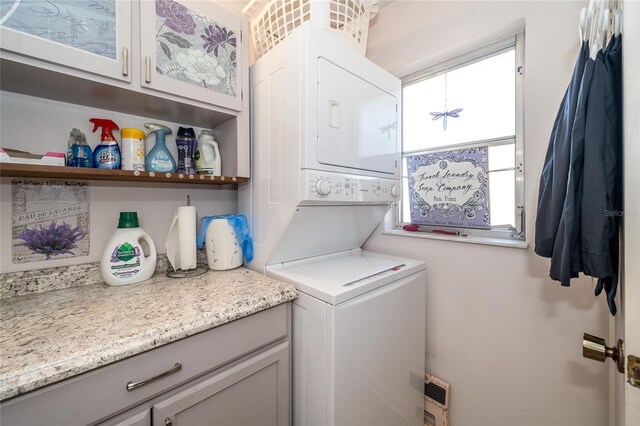 washroom featuring stacked washer / drying machine and cabinet space