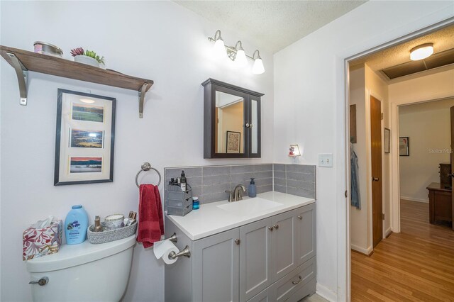 bathroom featuring toilet, wood finished floors, decorative backsplash, baseboards, and vanity