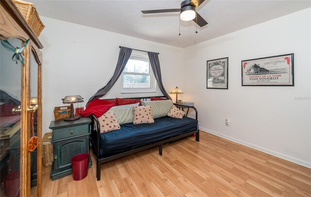 sitting room with light wood-style flooring, a textured ceiling, baseboards, and ceiling fan