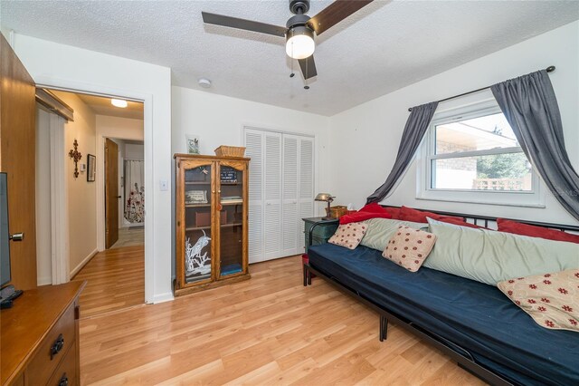 living room featuring light wood-style flooring, a ceiling fan, and a textured ceiling