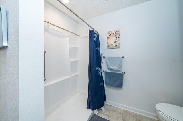 bathroom featuring toilet, a shower with curtain, baseboards, and a textured ceiling