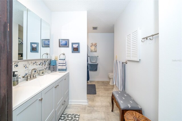 bathroom featuring visible vents, baseboards, toilet, vanity, and a textured ceiling