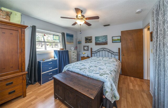 bedroom featuring ceiling fan, visible vents, a textured ceiling, and light wood-style flooring