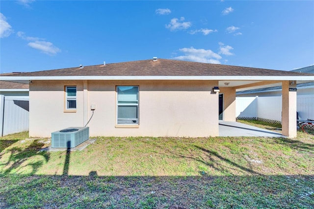 back of property featuring central AC unit, fence, a lawn, stucco siding, and a patio area