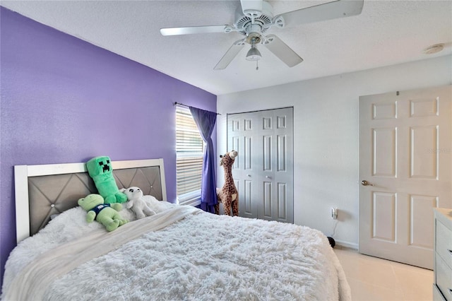 bedroom featuring light tile patterned floors, a textured ceiling, a ceiling fan, baseboards, and a closet