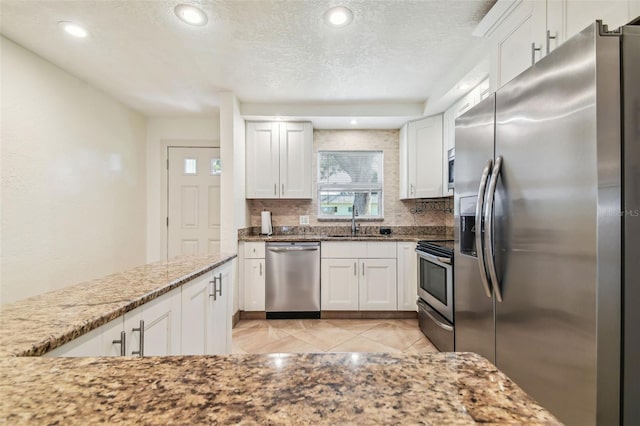 kitchen with white cabinetry, stainless steel appliances, light stone countertops, and sink