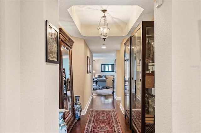 corridor with dark wood-style floors, a raised ceiling, and baseboards