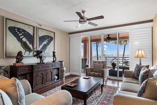 living area with dark wood-style floors, ceiling fan, baseboards, and a textured ceiling