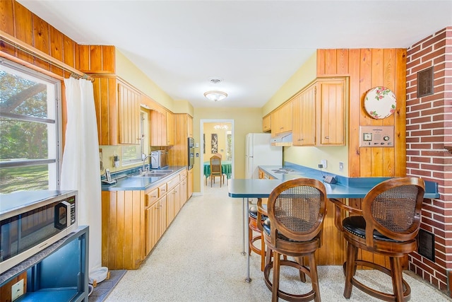 kitchen featuring light brown cabinetry, sink, wooden walls, and white refrigerator