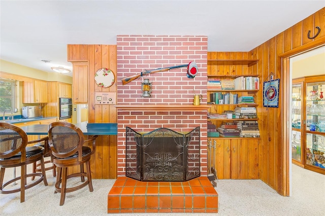 carpeted living room with wooden walls, sink, and a brick fireplace