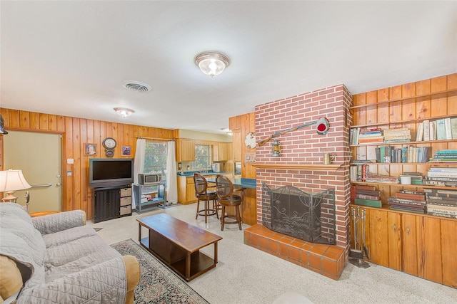 carpeted living room featuring a brick fireplace and wooden walls