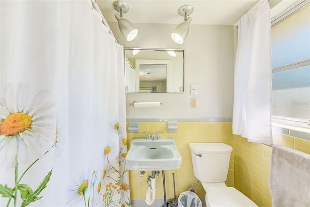 bathroom with toilet, sink, and tile walls