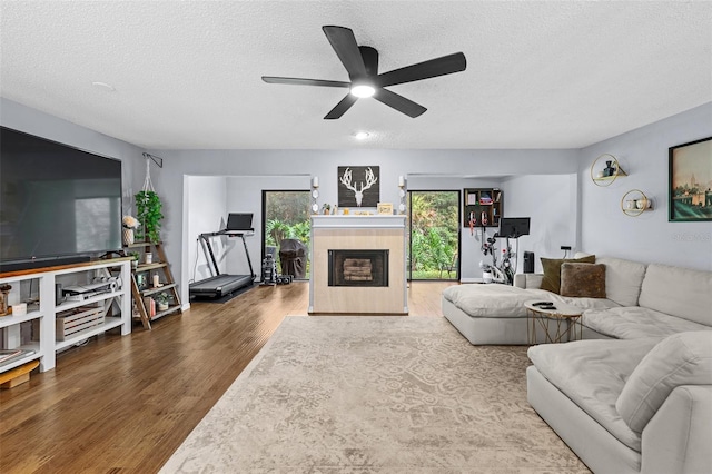 living room featuring ceiling fan, a textured ceiling, wood finished floors, and a tile fireplace